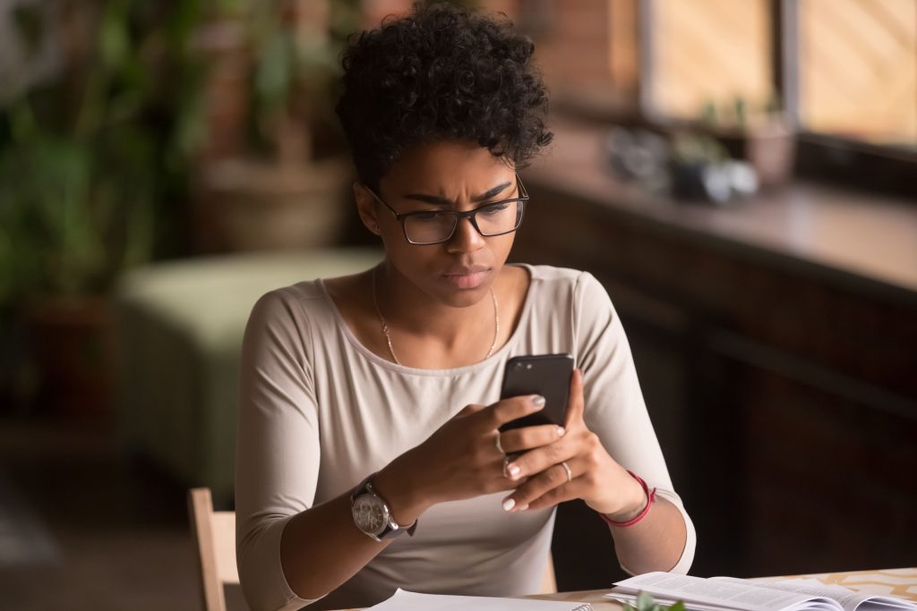 Woman sitting at a desk, frowning while looking at her cell phone