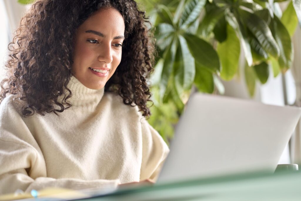 A woman is sitting behind her laptop and smiling.