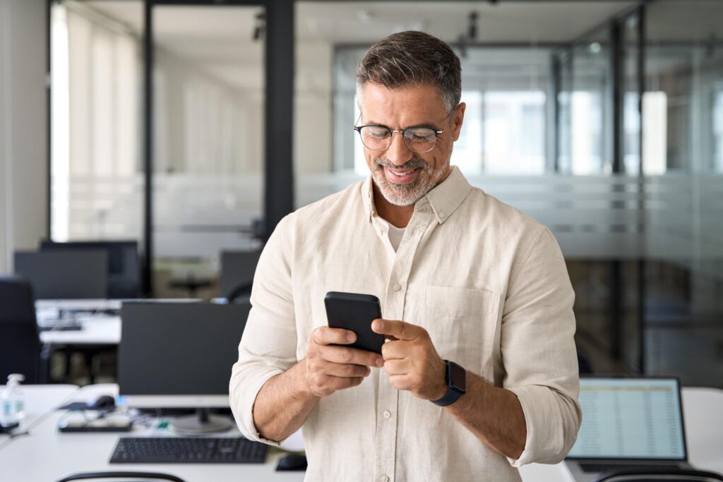A man in an office setting, focused on looking at his phone.