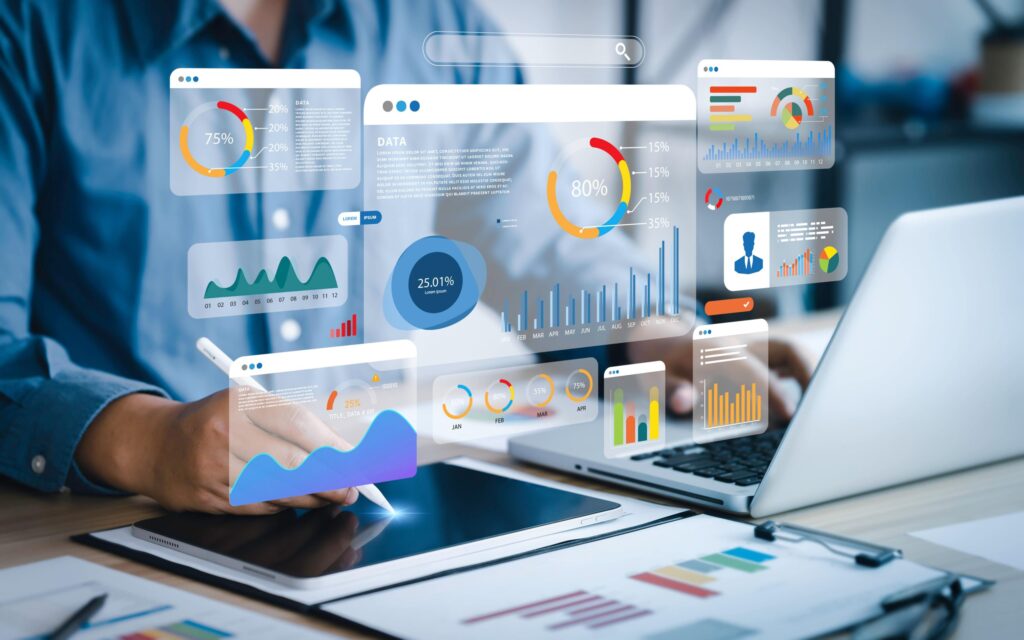The image shows a person working on a tablet and laptop with various interactive data visualizations and charts floating above the devices, representing data analysis and business intelligence.