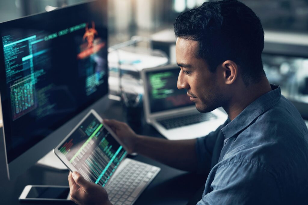 A man is seated at a computer with a script open, looking at data displayed on the laptop,
