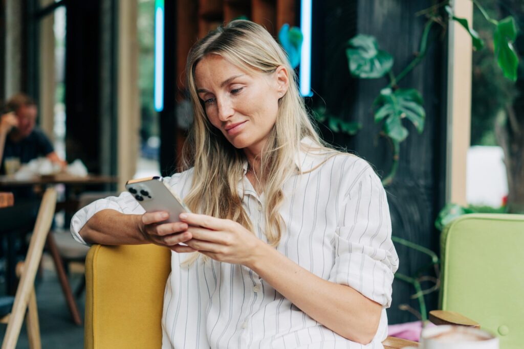 In a cafe, a woman is looking at her phone and smiling.