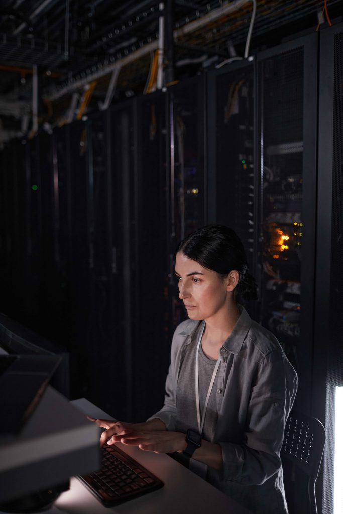 A woman in a dark room, focused on typing on her laptop screen.