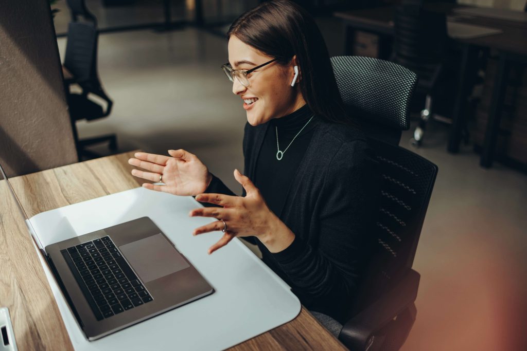 woman wearing earphones, seated behind her laptop in an office setting, engaged in a conversation during a business meeting.