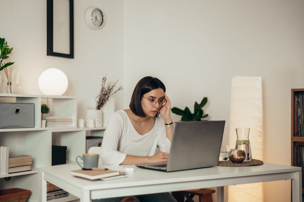 A woman with a struggled look is intently staring at her laptop screen.